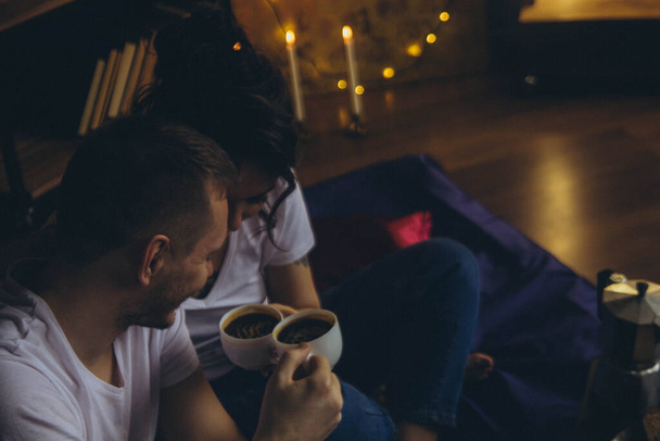 loving couple drinking coffee together in white cups in a dark room with candles, horizontal - Foto, Imagem