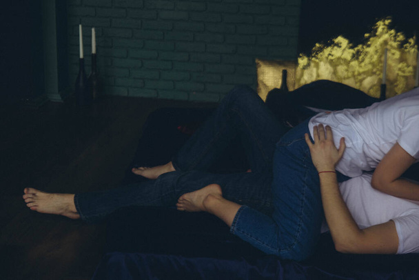 loving couple in white T-shirts and blue jeans lying on a mattress in a dark room, horizontal - Фото, зображення