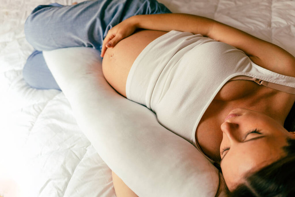 Schwangere Frau mit Schlafkissen. Junge werdende Mütter schlafen mit schwangeren Bauchstützkissen. Konzept der Schwangerschaft, Mutterschaft, Erwartung der Geburt - Foto, Bild