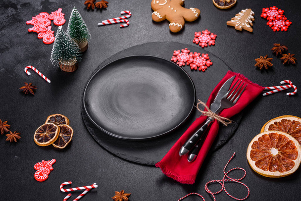 Christmas table setting with empty black ceramic plate, fir tree branch and black accessories on black stone background - Photo, Image
