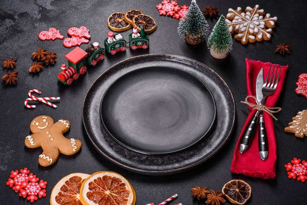 Christmas table setting with empty black ceramic plate, fir tree branch and black accessories on black stone background - Photo, Image