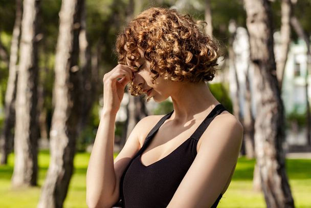Beautiful redhead woman wearing black sports bra standing on city park, outdoors rubbing nose and eyes feeling fatigue and headache. Stress and frustration concept. Massaging nose bridge. - Zdjęcie, obraz