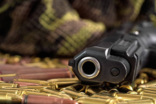 Yellow brass and brown bronze bullets, with black gun barrel near, closeup detail - Zdjęcie, obraz