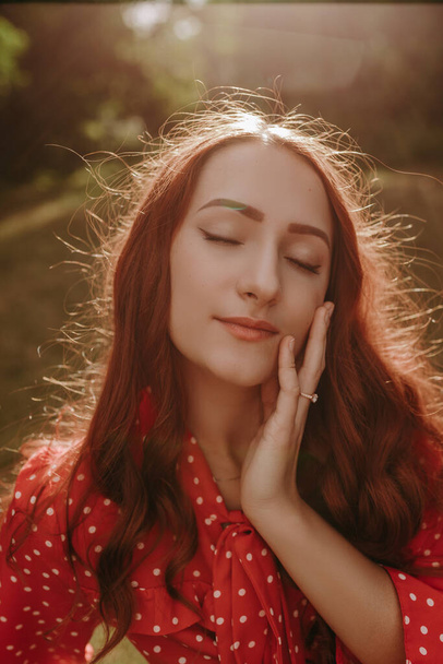Retrato de mujer pelirroja bonita al aire libre en la luz del atardecer. Modelo femenina tocando su cara a mano y ojos cerrados - Foto, Imagen