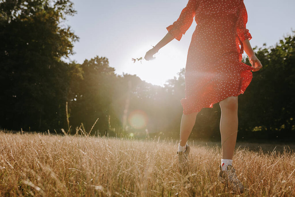 Mujer corriendo en el prado de hierba seca y sosteniendo en la mano una sola flor - Foto, Imagen