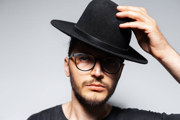 Close-up portrait of young serious handsome man wearing black hat and glasses. - Photo, Image