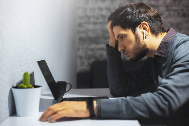 Side portrait of sad man, working online at home. Looking in laptop. - Φωτογραφία, εικόνα