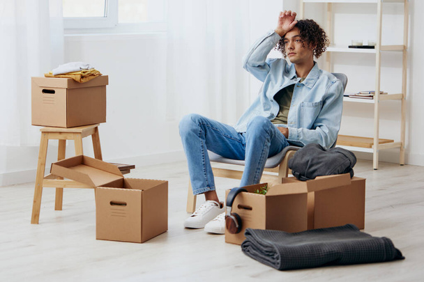 Un giovane seduto su una sedia che disfa le valigie con una scatola in mano che muove gli interni. Foto di alta qualità - Foto, immagini