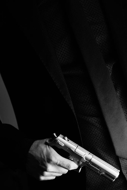 Ένας καλοντυμένος μυστικός πράκτορας ντετέκτιβ κατάσκοπος φοράει κοστούμι και γραβάτα κρατώντας αυτόματο πιστόλι.. - Φωτογραφία, εικόνα