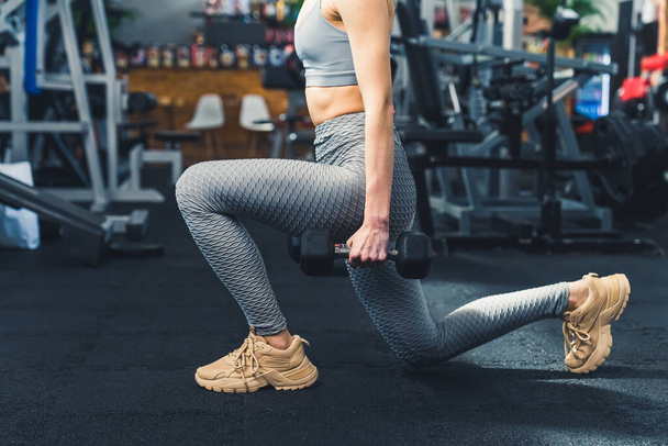 Lounge in bad position. Sporty Female Doing Deep Lunge Exercise Holding Two Dumbbells At The Gym. High quality photo - Photo, Image