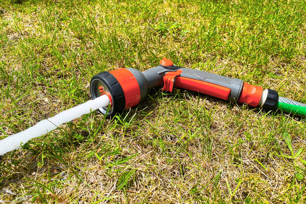 Bahçedeki çimlerin üzerinde su hortumu olan bir su tabancası. Bitkileri sulamak için bir fıskiye. - Fotoğraf, Görsel