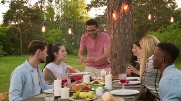 Group of modern multi-ethnic young men and women having fun together in park enjoying dinner celebrating something - Imágenes, Vídeo