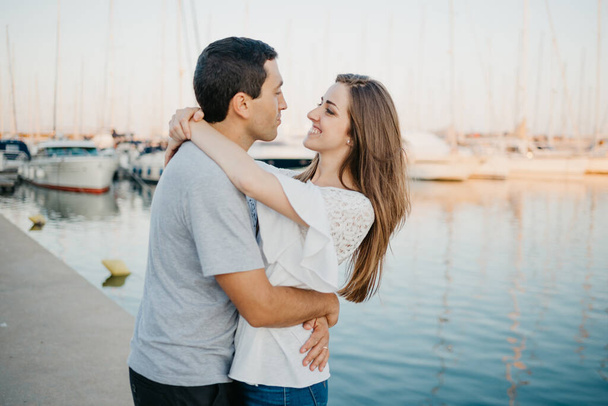 Un uomo ispanico sta abbracciando la sua felice ragazza bruna in porto in Spagna la sera. Un paio di turisti sono incontri vicino yacht al tramonto a Valencia. - Foto, immagini