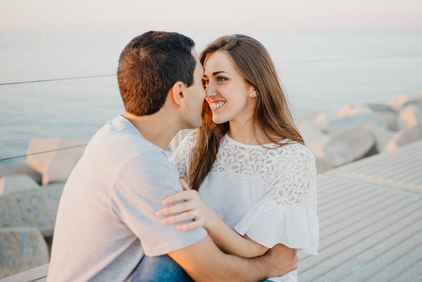 Un homme hispanique regarde sa copine brune souriante sur un brise-lames en Espagne dans la soirée. Quelques touristes à un rendez-vous au coucher du soleil à Valence. - Photo, image