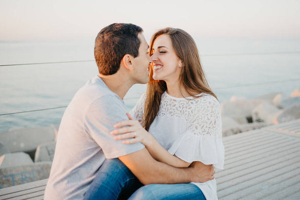 Een Spaanse man rommelt rond met zijn lachende brunette vriendin op een golfbreker in Spanje in de avond. Een paar toeristen op een date bij zonsondergang in Valencia. - Foto, afbeelding
