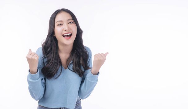 Joyful asian woman successful with excitement up keeps hands raised arm standing on white background with copy space. Excited young girl screaming success holding fist up looking camera over isolated. - Foto, Imagen