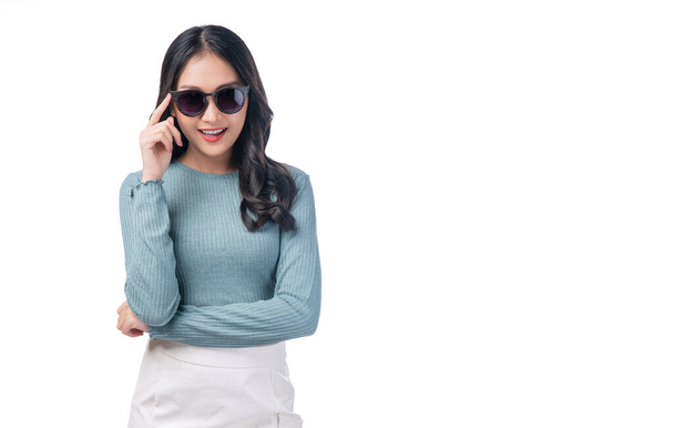 Portrait trendy asian woman wear sunglasses standing on white background. Gorgeous positive young lady holding hand on sunglasses laughing with copy space over isolated. Lifestyle summer concept. - Foto, imagen