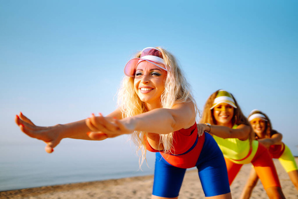 Három fürdőruhás lány edz a parton. Gyönyörű lányok táncolnak a parton. Fitness, tréning, aerobic és az emberek koncepciója. Aktív sport. - Fotó, kép