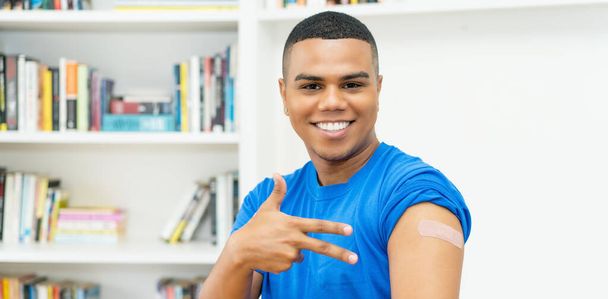 Handsome hispanic young adult man with plaster after vaccination against Covid 19 at doctors office - Foto, Imagen