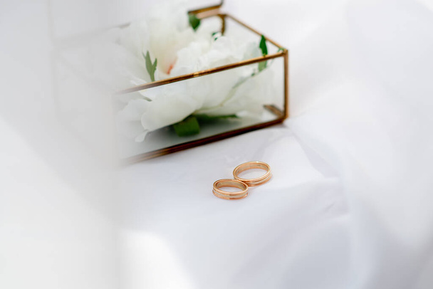 Goldene Eheringe auf dem Hintergrund einer Glasbox auf weißem Stoff. Konzept für Eventagenturen für die Zeremonie des Brautpaares - Foto, Bild
