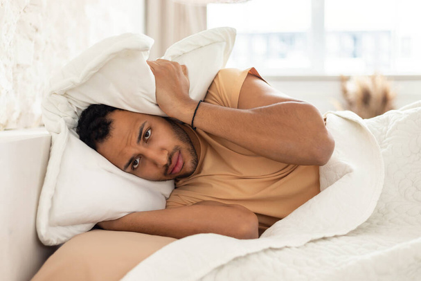 Unhappy Arabic Man Covering Head And Ears With Pillow Suffering From Headache And Noise, Having Insomnia In Modern Bedroom Indoors. Bad Soundproof At Home Concept - Fotoğraf, Görsel