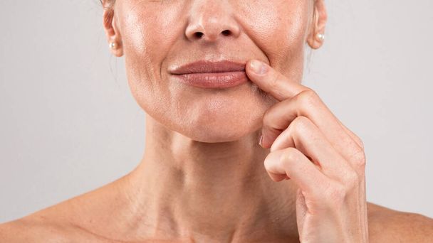 Closeup Shot Of Middle Aged Woman With Wrinkles On Face Touching Lips With Finger, Unrecognizable Mature Female With Bare Shoulders Posing Over Light Grey Studio Background, Free Space - Photo, Image