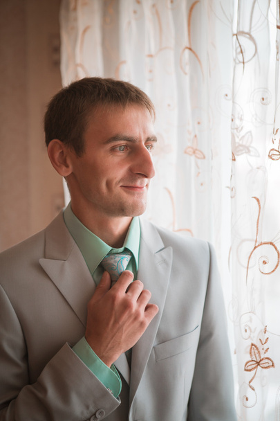 Портрет молодого жениха, завязывающего галстук во время подготовки к свадьбе
 - Фото, изображение