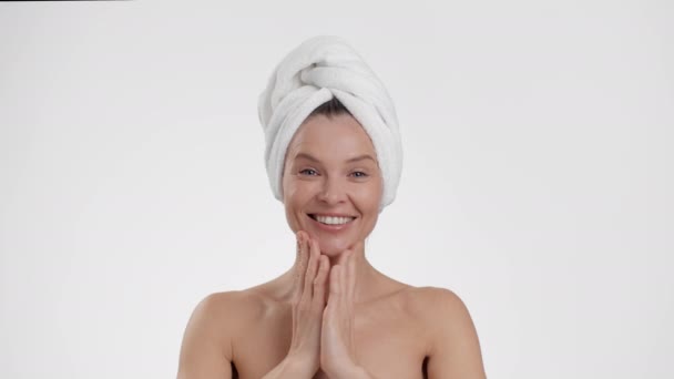 Rituais de cuidados de beleza no banheiro. Close up retrato de bela senhora de meia-idade feliz com toalha na cabeça fazendo massagem facebuilding após o chuveiro, fundo estúdio branco, câmera lenta - Filmagem, Vídeo
