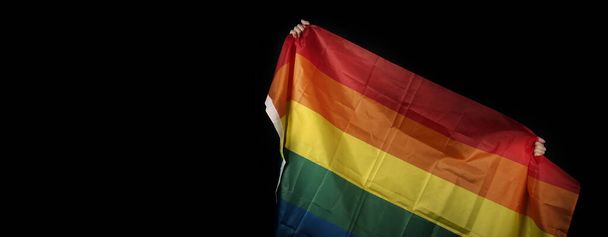 Flaga dumy LGBTQ na czarnym tle. Tęczowa flaga w gejowskich rękach. Reprezentują symbol wolności, pokoju, miłości i poszanowania różnorodności seksualnej. Lesbijki gej bii sexsual transgender queer. - Zdjęcie, obraz