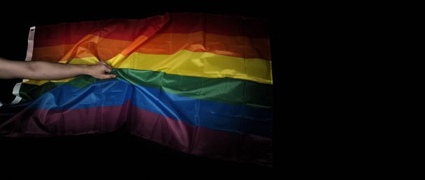 LMBTQ büszkeség zászló fekete háttérrel. Szivárvány zászló meleg kézben. A szabadság jelképe béke egyenlőség és szeretet és a szexualitás sokféleségének tiszteletben tartása. Leszbikus Meleg Bi Szexuális Transznemű Buzi. - Fotó, kép