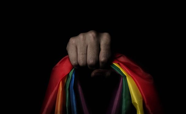 Гордость ЛГБТК на черном фоне. Радужный флаг в руке гея. Представляет собой символ свободы мира, равенства и любви и уважения разнообразия сексуальности. Lesbian Gay Bi sexsual Transgender Queer. - Фото, изображение