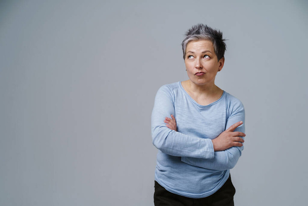 Pensive, thoughtful, doubt mature woman with grey hair in 50s posing with hands folded and copy space on left isolated on white background. Place for product placement. Aged beauty. Toned image. - Fotó, kép