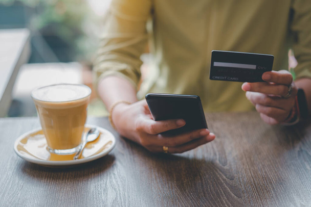 Les femmes détiennent une carte de crédit et utilisent leur téléphone portable pour payer leurs achats en ligne dans un café. Paiement en ligne Concept. - Photo, image