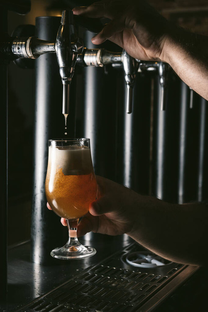 Primo piano della mano del barman al rubinetto della birra che versa una birra lager alla spina
 - Foto, immagini