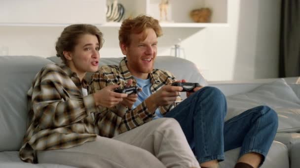 A barátok videojátékoznak a nappaliban. A boldog család élvezi a versenyt. Ginger férfi férj beszél mosolygó feleség szórakozik joysticks haza. Izgatott diákok pihennek együtt töltenek egy kis időt - Felvétel, videó