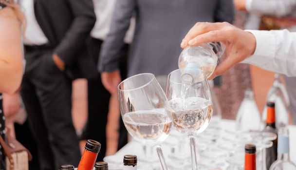 Zbliżenie rąk kelnera nalewających kieliszki do wina. Imprezy plenerowe, catering, spotkania robocze - Zdjęcie, obraz