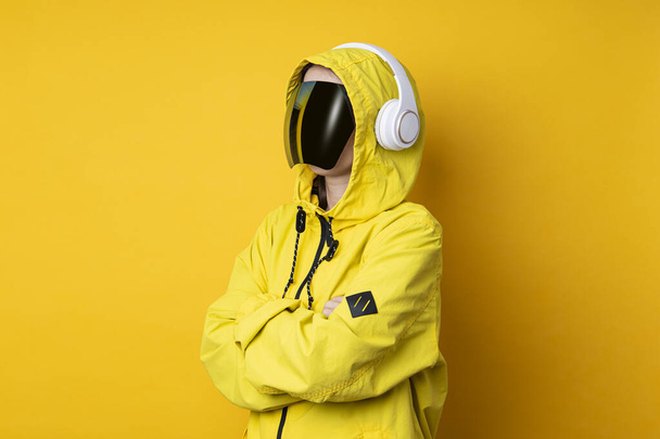 Młoda kobieta w okularach cyberpunkowych maska ze słuchawkami w żółtej kurtce na żółtym tle. - Zdjęcie, obraz