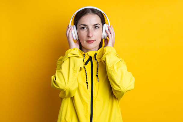 Mladá žena ve sluchátkách ve žluté bundě na žlutém pozadí - Fotografie, Obrázek