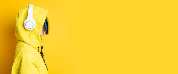 Młoda kobieta w cyberpunkowych okularach ze słuchawkami w żółtej kurtce na żółtym tle. Sztandar. - Zdjęcie, obraz