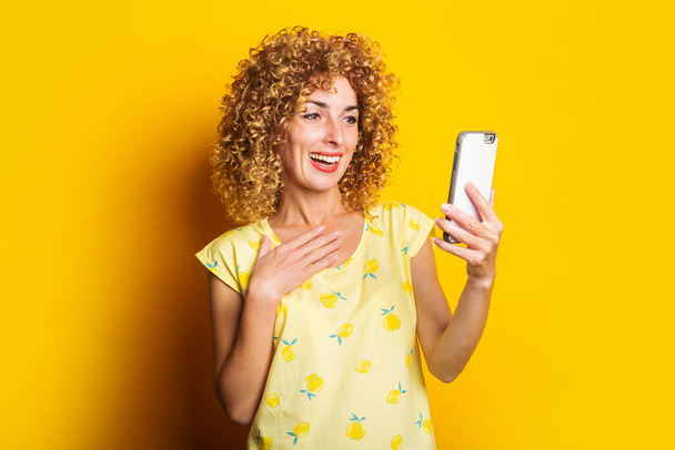 rizado joven mujer hablando en video chat en el teléfono sobre un fondo amarillo - Foto, Imagen