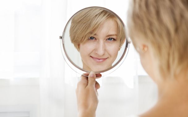 Beautiful healthy young woman looking in the mirror - Foto, afbeelding