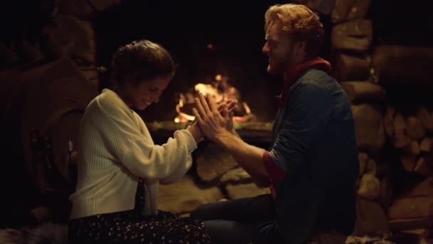 Loving couple warming fireplace in country house. Affectionate boyfriend girlfriend kiss hand on winter holidays close up. Romantic lovers express show love tenderness indoors. Cozy relax concept - Footage, Video
