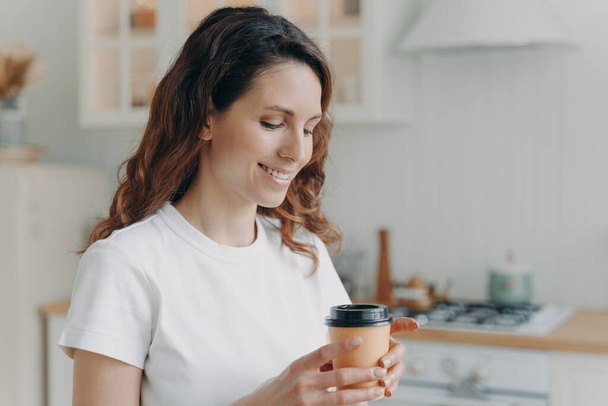 Relaxed happy woman with cup of coffee at home. Daily routine. Young attractive housewife alone at kitchen in morning. Scandinavian stylish interior. White modern furniture. - Photo, Image