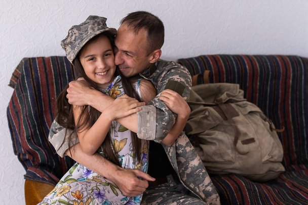 Μικρό παιδί είναι πολύ χαρούμενος ο πατέρας της ήρθε πίσω από το στρατό. Μικρό παιδί αγκαλιάζει τον πατέρα της. - Φωτογραφία, εικόνα