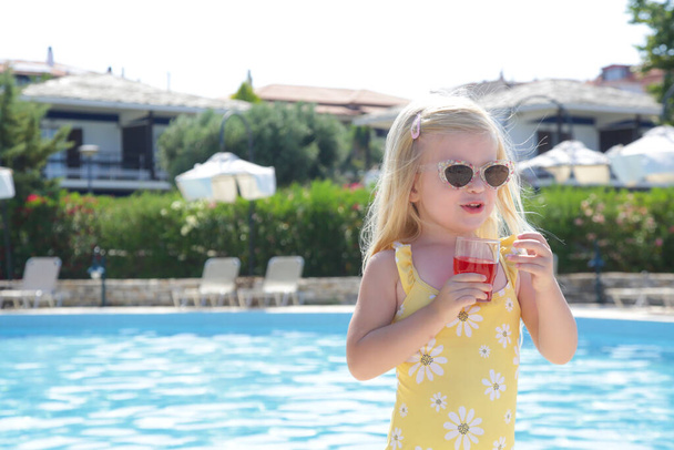 Дитина тримає склянку соку на краю басейну. Гідратація під час теплової хвилі
. - Фото, зображення