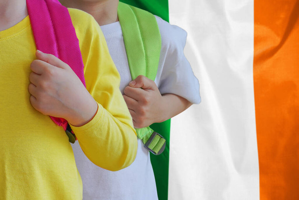 Two children with satchels background of Ireland flag. The concept of raising and educating children in Ireland - 写真・画像