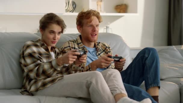Egy boldog pár, akik joystickokat tartanak a videojátékban. A feldúlt játékosok a kanapén pihennek. Koncentrált izgatott játékosok beszélnek online torna játék. Vörös hajú férfi gyönyörű nő használ gamepads otthon. - Felvétel, videó