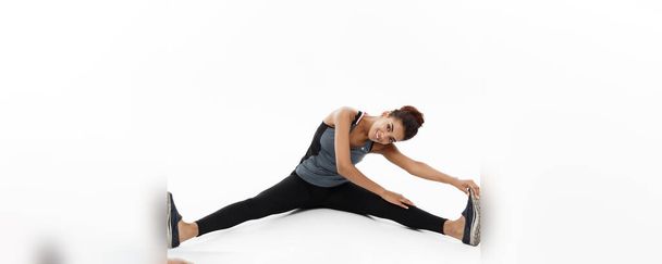 Sport, entraînement, mode de vie et concept Fitness - portrait d'une belle afro-américaine heureuse qui étire la jambe en s'asseyant. Isolé sur fond de studio blanc
 - Photo, image
