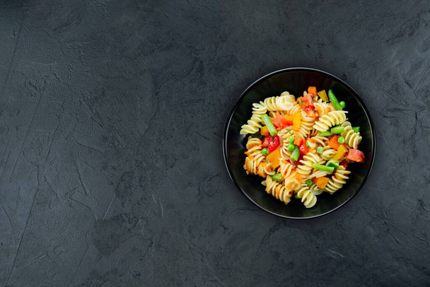 Penne pasta with vegetables, asparagus, peas, bell pepper, tomato, sauce, mozzarella cheese on a black background. Italian pasta with vegetables and seasoning on a dark background.Copy space.Flat lay. - Foto, Imagen