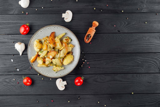Fried potatoes with mushrooms and tomatoes on a black background with spices. Delicious potatoes with vegetables and spices. - Фото, изображение